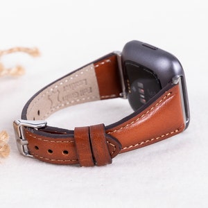 May include: A brown leather watch strap with white stitching. The strap is attached to a silver smartwatch with a black screen.