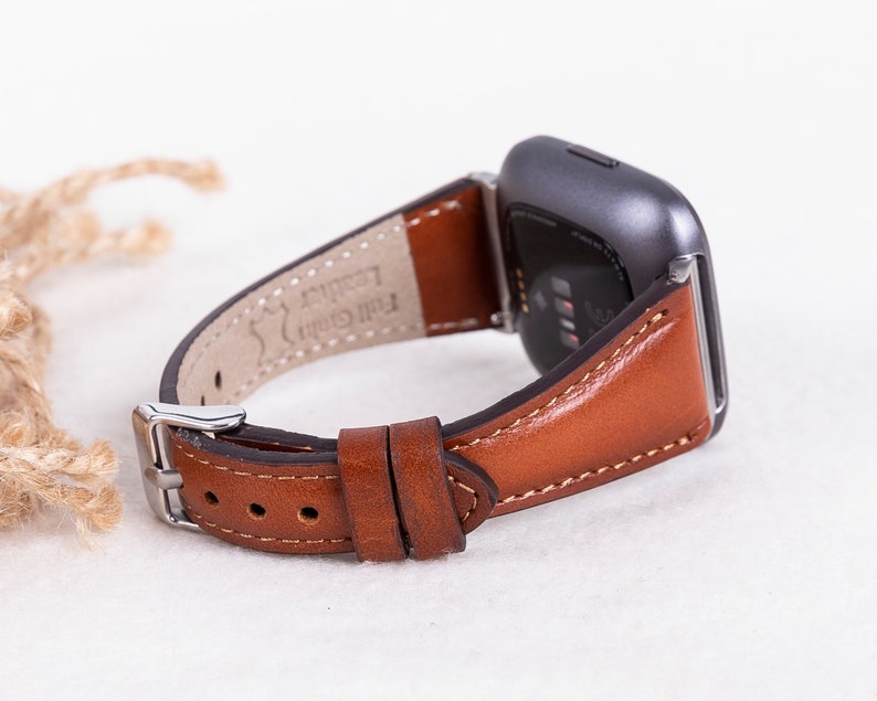 May include: A brown leather watch strap with white stitching. The strap is attached to a silver smartwatch with a black screen.