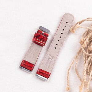 May include: Two red leather watch straps with silver buckles. The strap on the left has a crocodile pattern. The strap on the right has the text "Full Grain Leather" printed on it.