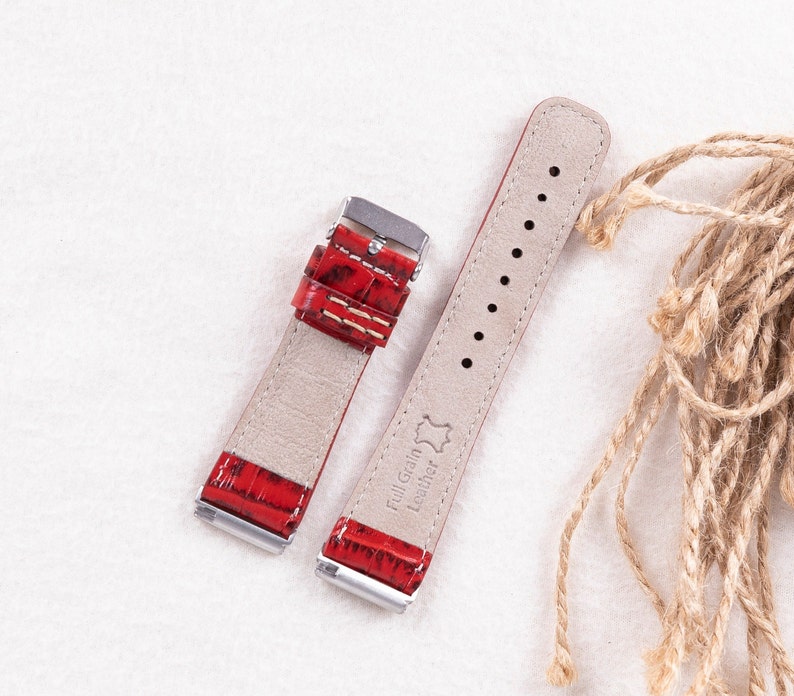 May include: Two red leather watch straps with silver buckles. The strap on the left has a crocodile pattern. The strap on the right has the text "Full Grain Leather" printed on it.