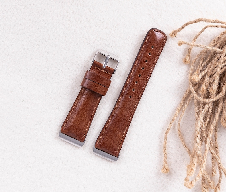 May include: Two brown leather watch straps with silver buckles. The straps have stitching along the edges and are laid out on a white surface.