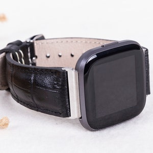 May include: A black leather watch band with a silver buckle and a black square smartwatch with a black screen.