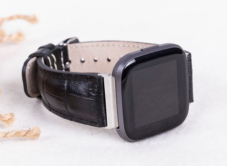 May include: A black leather watch band with a silver buckle and a black square smartwatch with a black screen.