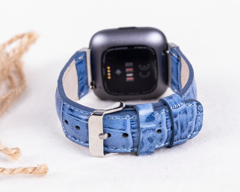 Puede incluir: Una correa de reloj de cuero azul claro con una hebilla plateada. La correa est&aacute; dise&ntilde;ada para un reloj inteligente Fitbit.