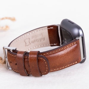 May include: A brown leather watch band with a silver buckle. The band is labeled "Full Grain Leather".