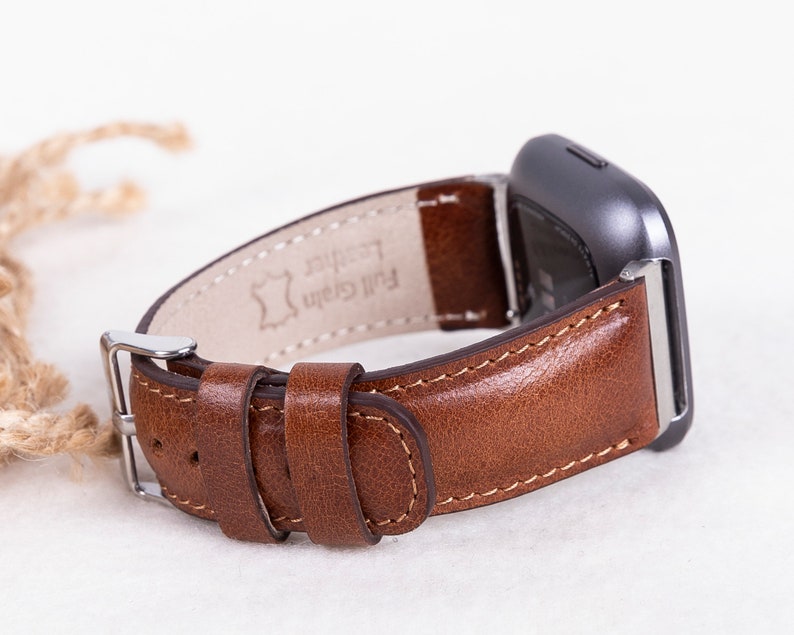 May include: A brown leather watch band with a silver buckle. The band is labeled "Full Grain Leather".