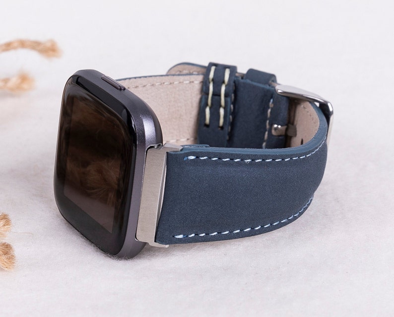 May include: A dark blue leather watch band with white stitching for a smartwatch. The band is made of soft, supple leather and has a classic look.