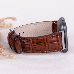 May include: A brown leather watch band with a crocodile pattern. The band is attached to a silver watch face.