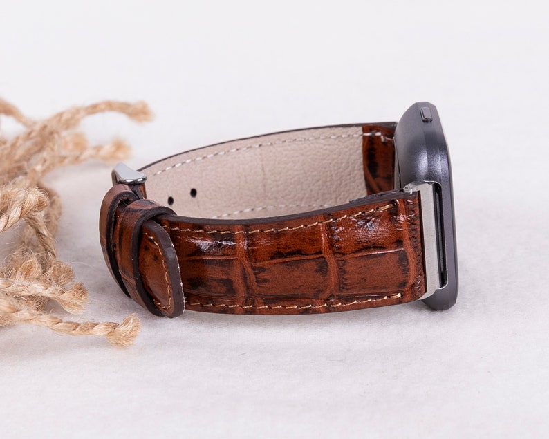 May include: A brown leather watch band with a crocodile pattern. The band is attached to a silver watch face.
