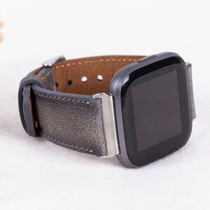 May include: A gray leather watch band with a silver buckle and a black smartwatch with a square face.
