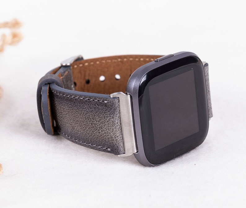 May include: A gray leather watch band with a silver buckle and a black smartwatch with a square face.