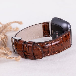 May include: A brown leather watch band with a crocodile pattern. The band is attached to a silver watch face.