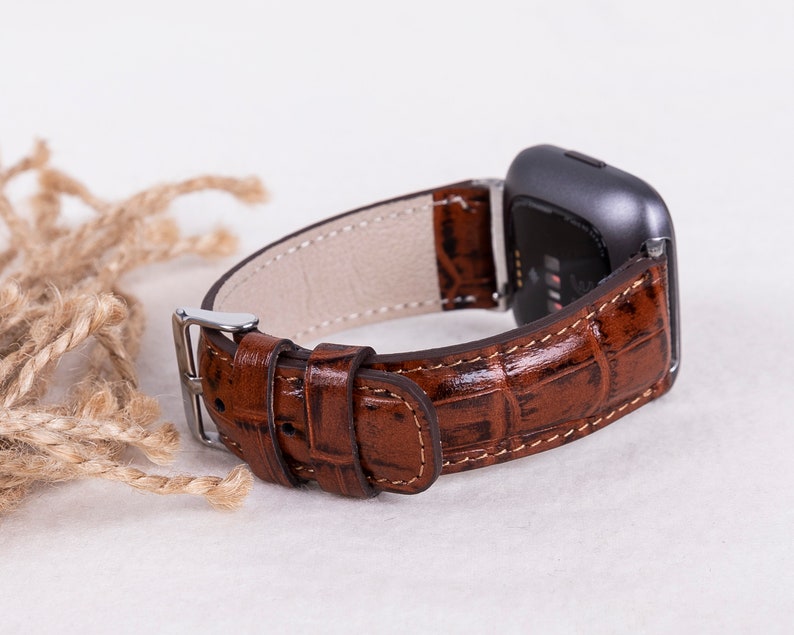 May include: A brown leather watch band with a crocodile pattern. The band is attached to a silver watch face.