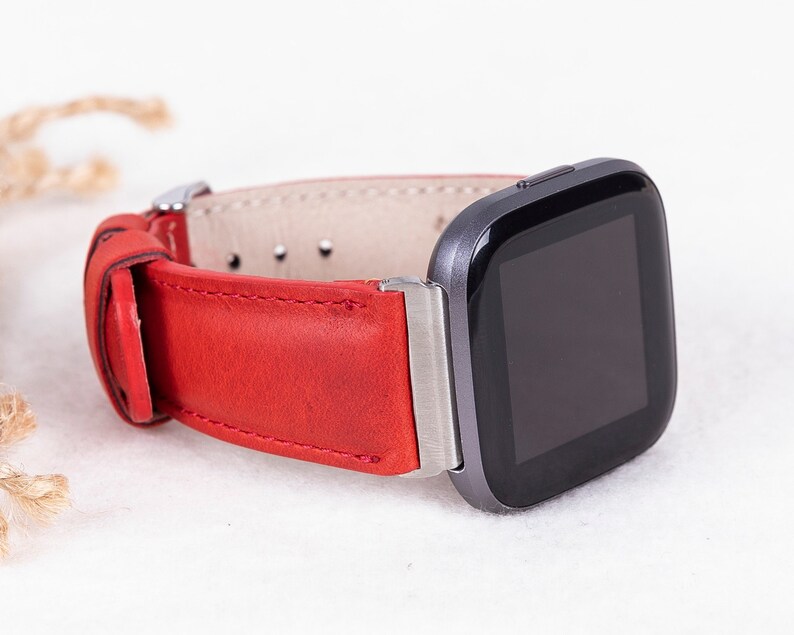 Puede incluir: Una correa de reloj de cuero rojo con una hebilla plateada, unida a un reloj inteligente negro con una cara cuadrada.