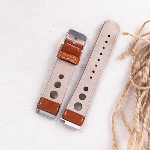 May include: Two brown leather watch straps with white stitching and silver buckles. One strap has a perforated design and the other has a smooth surface.