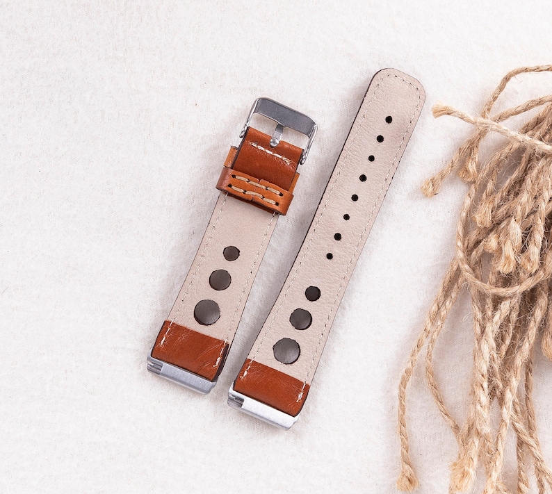 May include: Two brown leather watch straps with white stitching and silver buckles. One strap has a perforated design and the other has a smooth surface.