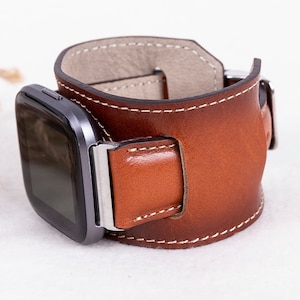 K&ouml;nnte beinhalten: Ein braunes Lederarmband mit wei&szlig;en N&auml;hten. Das Armband ist f&uuml;r eine quadratische Smartwatch konzipiert.
