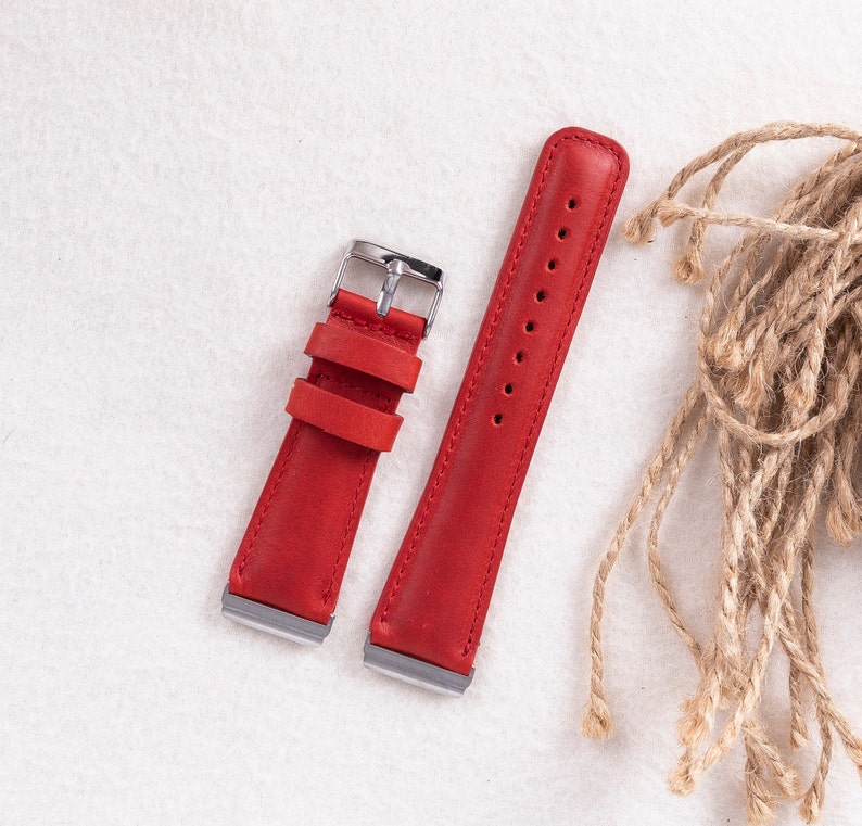Puede incluir: Dos correas de reloj de cuero rojo con hebillas plateadas. Las correas est&aacute;n sobre una superficie blanca.