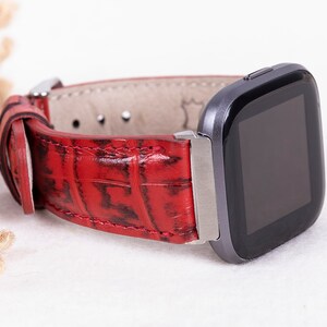 May include: Red leather watch band with a crocodile pattern. The band is attached to a black and silver smartwatch.