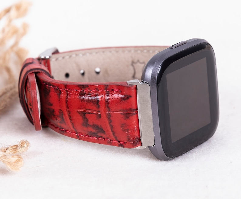 May include: Red leather watch band with a crocodile pattern. The band is attached to a black and silver smartwatch.