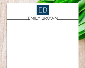Könnte beinhalten: Weißes Briefpapier mit einem marineblauen Quadrat mit den Initialen "EB" und dem Namen "EMILY BROWN" in einer Serifenschrift. Eine dünne marineblaue Linie trennt den Namen vom leeren Raum darunter. Das Briefpapier liegt auf einer hellen Holzoberfläche.