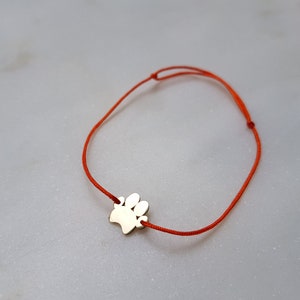 Könnte beinhalten: Ein rotes Armband mit einem silbernen Pfotenabdruck-Anhänger.