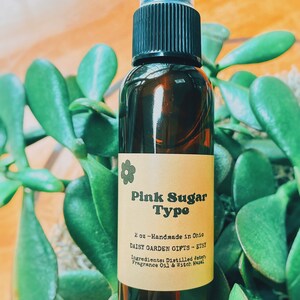 May include: A brown glass bottle with a black spray top and a label that reads "Pink Sugar Type" with the text "2 oz - Handmade in Ohio Daisy Garden Gifts - Etsy Ingredients: Distilled Water, Fragrance Oil & Witch Hazel".