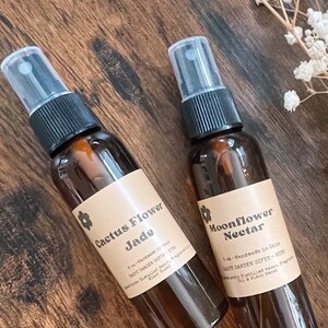 May include: Two amber glass spray bottles with brown paper labels. The labels have a floral design and text that reads "Cactus Flower Jade" and "Moonflower Nectar". Both bottles are 1 oz and handmade in Chile.