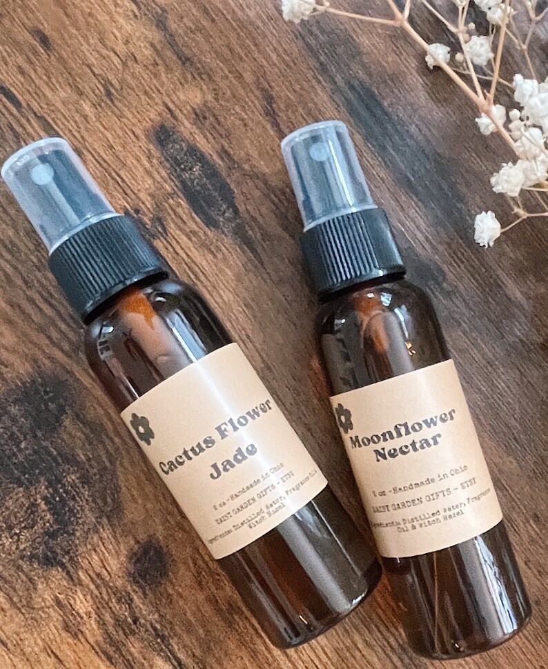 May include: Two amber glass spray bottles with brown paper labels. The labels have a floral design and text that reads "Cactus Flower Jade" and "Moonflower Nectar". Both bottles are 1 oz and handmade in Chile.