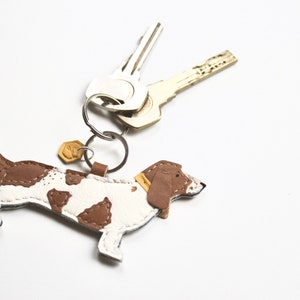 May include: A brown and white leather dachshund keyring with a gold-coloured key ring and two silver keys.