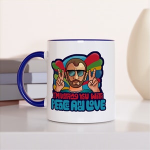 Puede incluir: Taza de cerámica blanca con borde y asa azules. La taza presenta una ilustración de dibujos animados de un hombre con gafas de sol y barba, haciendo un signo de paz con ambas manos. El texto "I'm giving you with peace and love" está impreso en una fuente retro colorida.