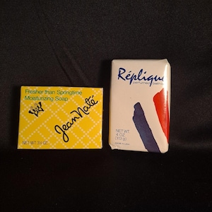 May include: A yellow rectangular box of Jean Naté Fresher than Springtime Moisturizing Soap with a butterfly graphic and a white rectangular box of Réplique perfumed bath soap featuring blue and red abstract shapes and a net weight of 4 oz.