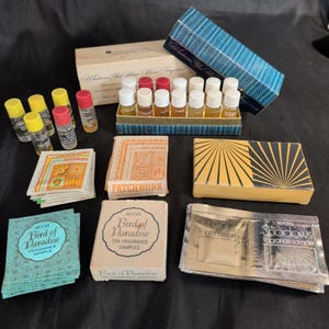 Può includere: Una collezione di campioni di profumo Avon vintage che include piccole fiale di vetro con tappi colorati, scatole di cartone etichettate Patchwork e Bird of Paradise, e bustine di alluminio etichettate Lights e Shadows.
