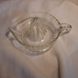 Peut inclure: Un presse-agrumes en verre transparent doté d'un cône central, d'un bassin circulaire avec des détails nervurés verticaux sur les parois extérieures, d'un petit bec verseur sur un côté et d'une poignée robuste fixée au bord opposé.