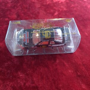 May include: A black die-cast stock car model inside a clear plastic display box. The car features the number 40 in gold, the text UAW-GM QUALITY 500, PROGRAM CAR, and CHARLOTTE, with the date OCTOBER 16, 1999 printed on the roof and side panels.