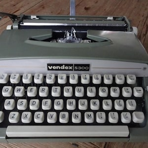 May include: A green and white vintage typewriter with the brand name "vendex s300" printed on the front. The typewriter has a standard QWERTY keyboard.