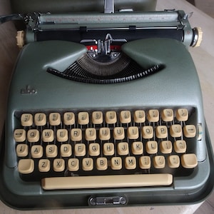 May include: A vintage green typewriter with a cream-coloured keyboard and a black carriage return lever. The typewriter has the word "Olivetti" printed on the front.