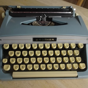 May include: A blue Brother typewriter with a yellow keyboard. The typewriter has a carriage return lever on the left side and a tab key on the right side.