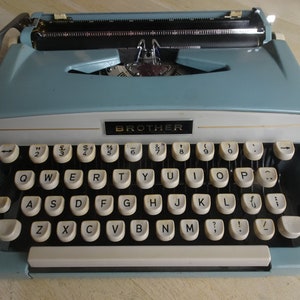 May include: A light blue Brother typewriter with a white and black keyboard. The keys have white lettering and the typewriter has a gold trim.