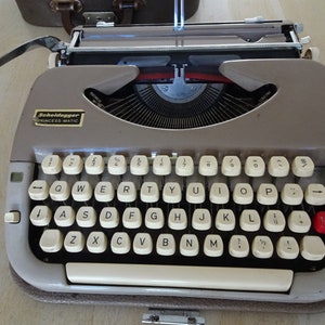 May include: A gray Scheidegger Princess Matic typewriter with a white keyboard and red tab key.