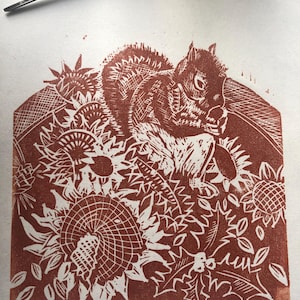 May include: A red and white linocut print of a squirrel sitting in a field of sunflowers. The print is titled "Squirrel and Sunflowers" and signed "RYE 2023".