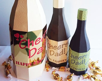 Pode incluir: Três caixas de garrafa de champanhe de papel artesanal em papel dourado, branco e preto. As caixas são decoradas com o texto "Cheers Dad!" e "Happy Father's Day".