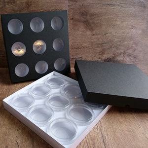 Może przedstawiać: Czarne pudełko z dziewięcioma okrągłymi przegródkami i białe pudełko z dziewięcioma okrągłymi przegródkami, oba pudełka są otwarte, a białe pudełko znajduje się na czarnym pudełku.