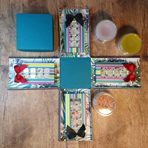 May include: A teal green box with a floral design and a white and red striped pattern. The box is open to reveal a set of wax melts in a variety of colours. The box also includes a small jar of bath salts and a small jar of lotion.