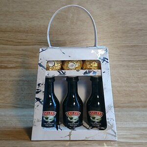 Pode incluir: Uma sacola de presente branca com al&ccedil;a, com um padr&atilde;o de m&aacute;rmore e uma janela transparente. Dentro da sacola, tr&ecirc;s garrafas em miniatura de Baileys Irish Cream e alguns chocolates embrulhados em ouro.