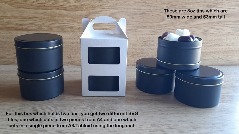 May include: Two black metal tins with gold trim, stacked on top of each other. The tins are 8 ounces and measure 80mm wide and 53mm tall. A white cardboard box with a handle and two cut-out windows is also shown. The text "These are 8oz tins which are 80mm wide and 53mm tall" is visible in the image.