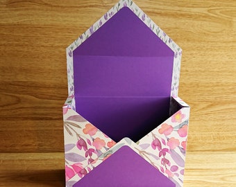 Pode incluir: Uma caixa com padrão floral branco e roxo com uma tampa roxa. A caixa está aberta e o interior é roxo.