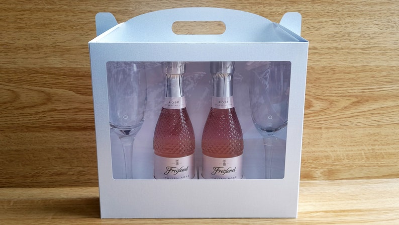 May include: A white gift box with a clear window showing two small bottles of pink Italian rose sparkling wine and two champagne flutes.