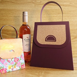 Pode incluir: Duas sacolas de presente com al&ccedil;as, uma com um padr&atilde;o floral e a outra com um design marrom e dourado. Uma garrafa de vinho branco Grenache da Gallo Family Vineyards est&aacute; no fundo.