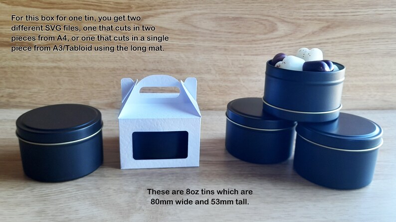 May include: A white cardboard box with a window and a handle, next to three black metal tins. The tins are 8 ounces and measure 80mm wide and 53mm tall. The text on the image reads: "For this box for one tin, you get two different SVG files, one that cuts in two pieces from A4, or one that cuts in a single piece from A3/Tabloid using the long mat. These are 8oz tins which are 80mm wide and 53mm tall."